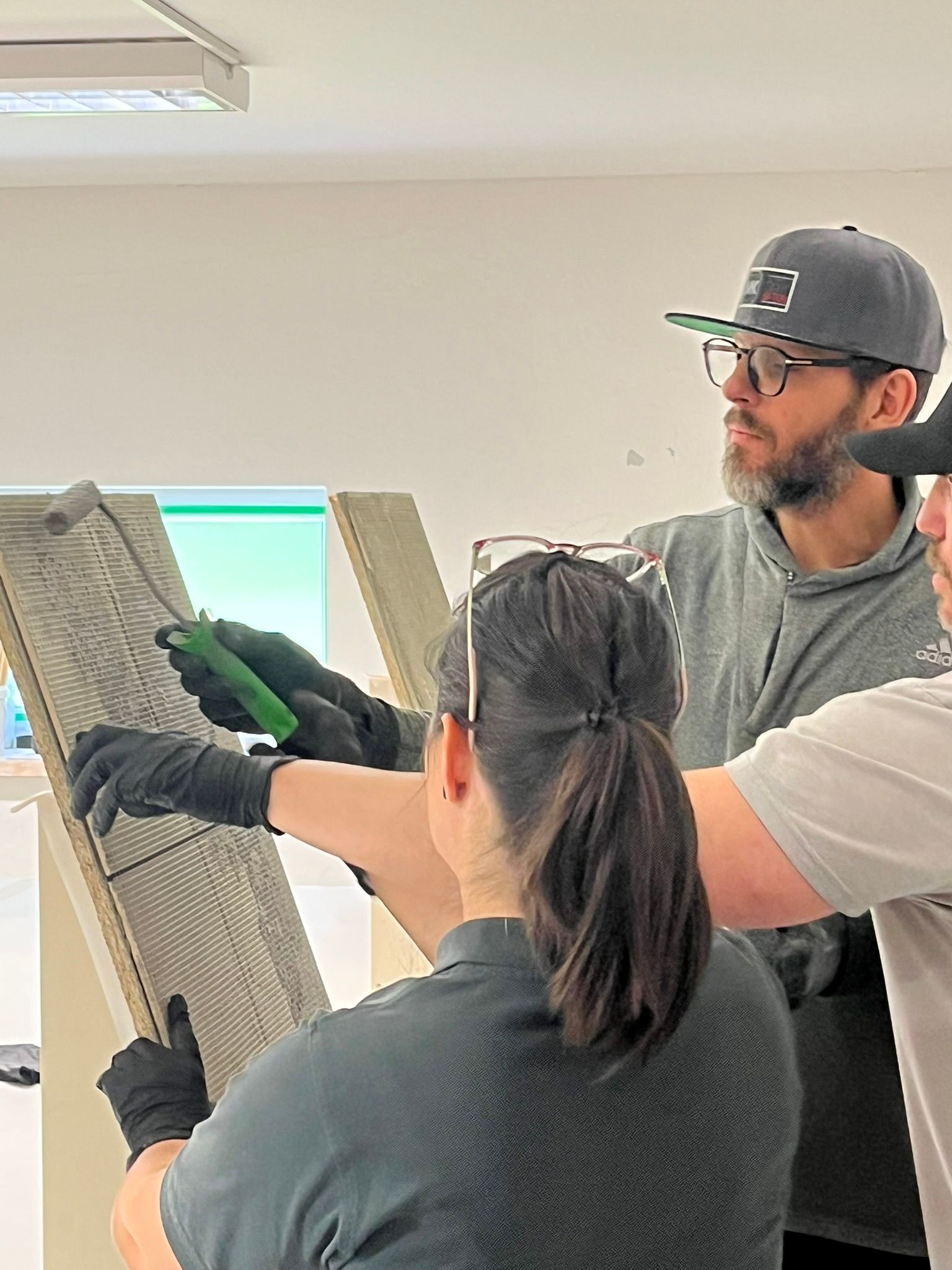 Workshop-Teilnehmende tragen fugenlose Oberflächenmasse mit Walze und Spachtel auf ein Musterbrett auf