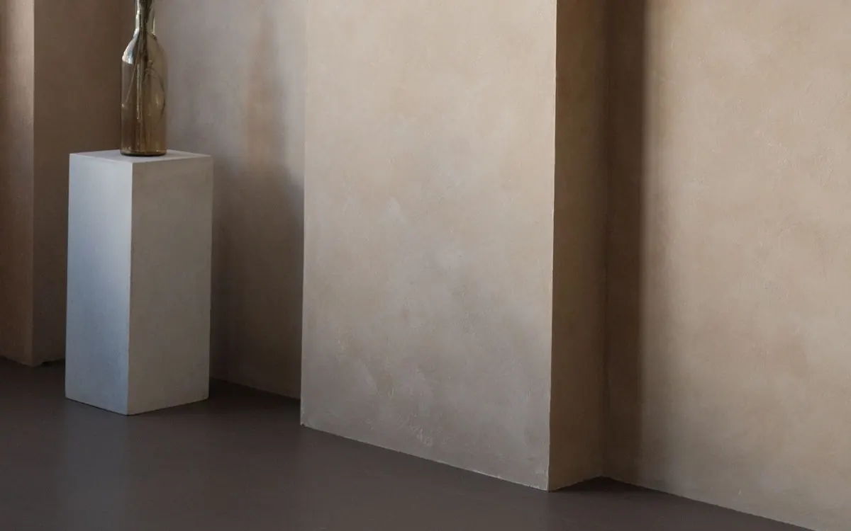 Fugenlos verputzte Wand in warmem Sandton mit Wandvorsprung, davor ein weißer Sockel mit Vase