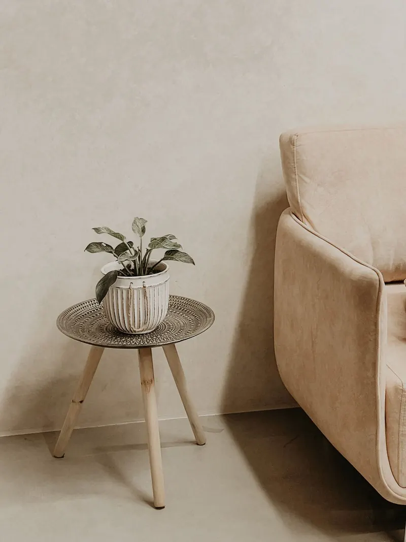 Wohnzimmerecke mit fugenloser, warm-beiger Wand und nahtlosem Boden, Sessel und Beistelltisch mit Pflanze
