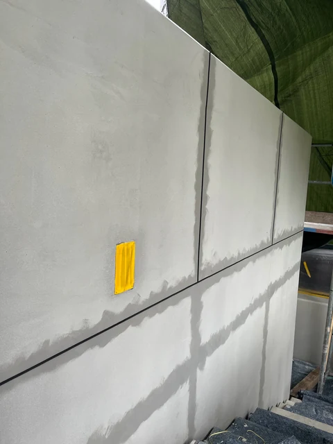Gespachtelte Mauer mit dunklen, abgeklebten Fugen im Raster, die oberen Felder schon beschichtet, an einer Fuge eine gelbe Markierung