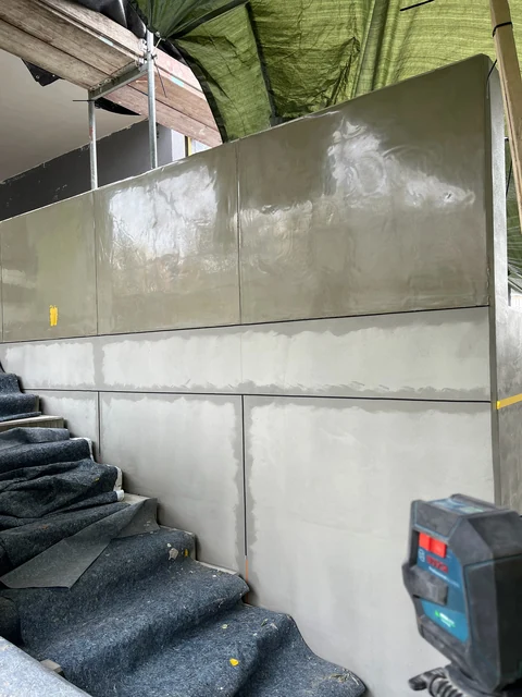 Mauer mit Fugenraster an einer Außentreppe: Die oberen Felder glänzen unter frisch aufgelegter Schalbetonfolie, die unteren Felder zeigen noch den grauen Grundspachtel