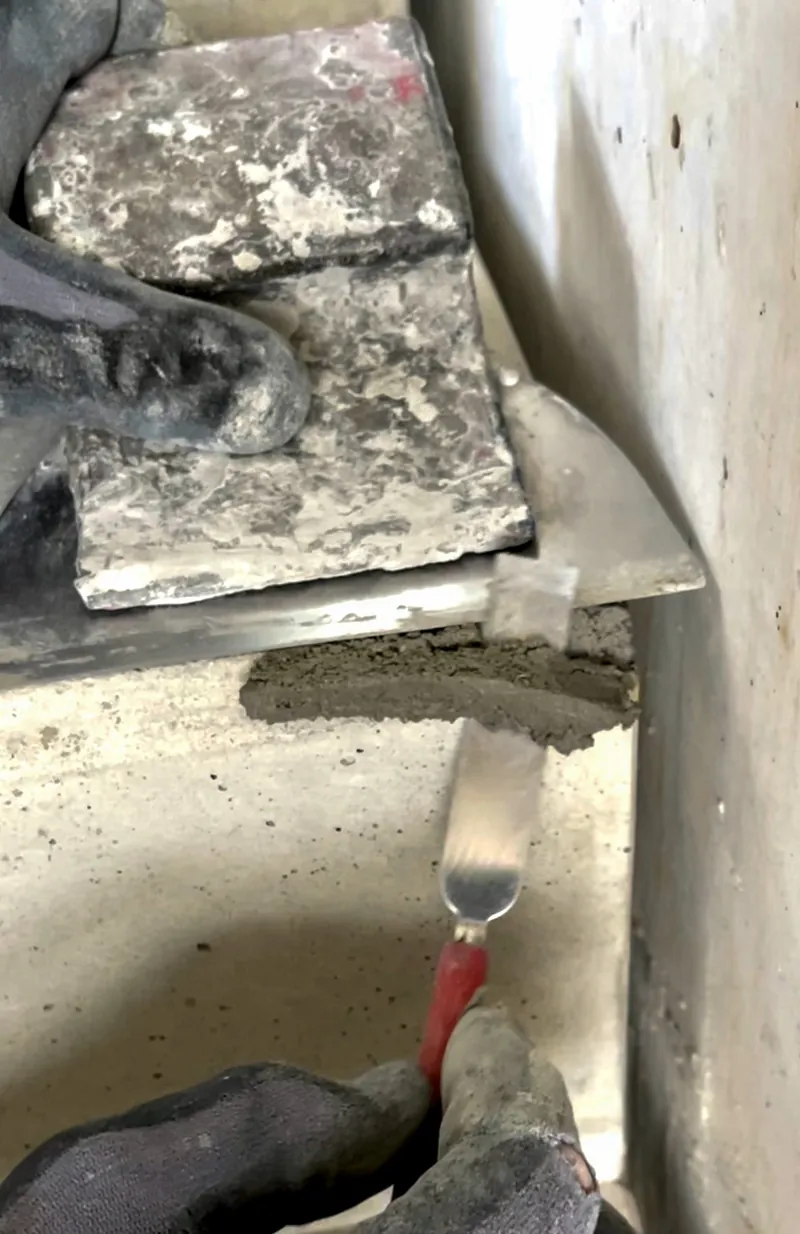 Hände mit Glättkelle und Spachtel bauen eine Betonkante in einer Ecke auf