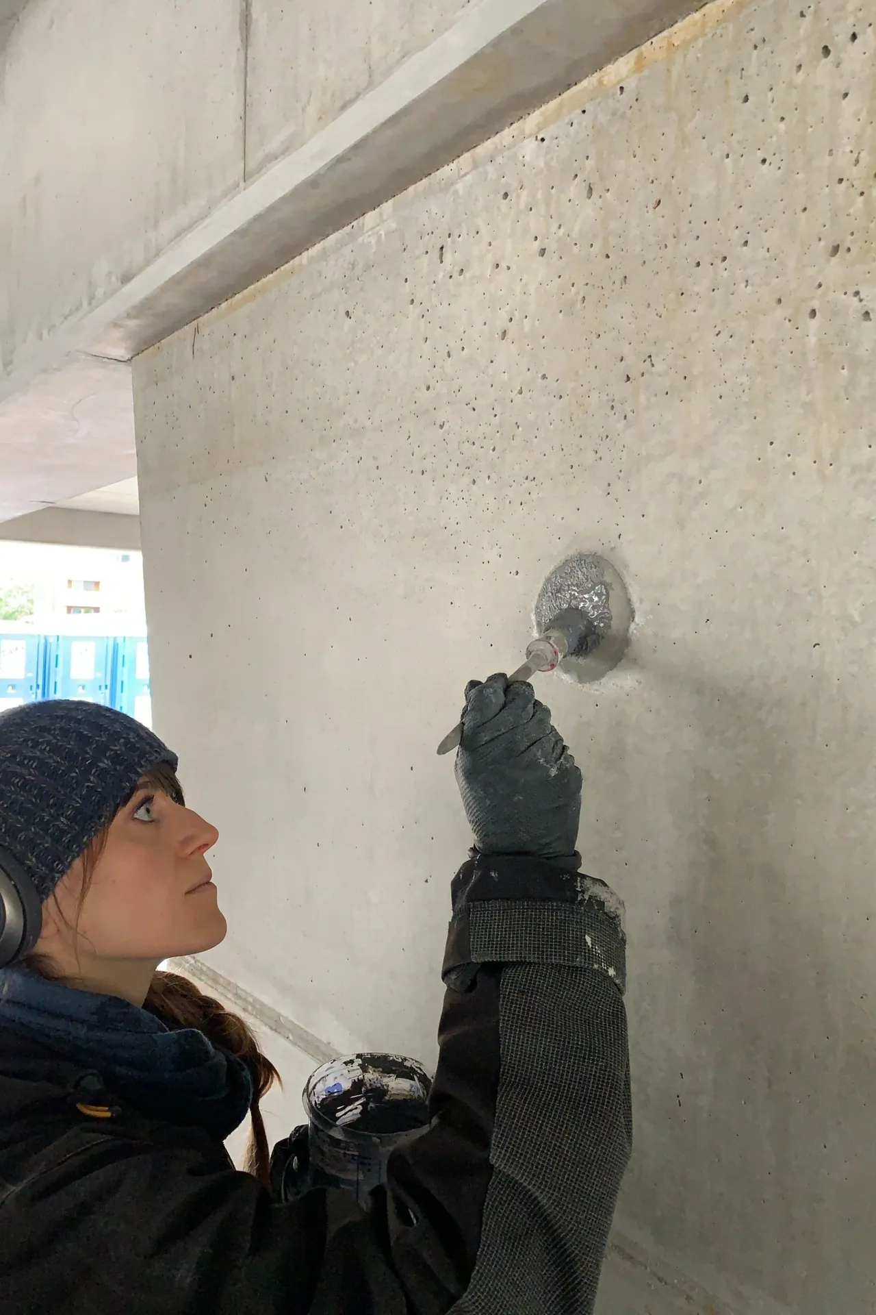 Mitarbeiterin schließt mit einem Spachtel einen Lunker in einer Sichtbetonwand