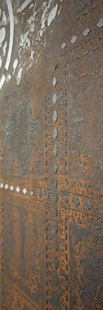 Wand in Rostoptik aus der Nähe mit Schablonenmustern aus Punktlinien und Rauten, oben der Rand eines weißen Ornaments