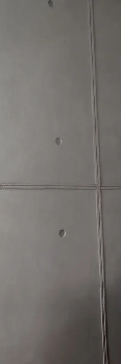 Ausschnitt einer Wand in Schalbetonoptik in einer Wohnung, graue Platten mit feinen Plattenfugen und runden Ankerlöchern