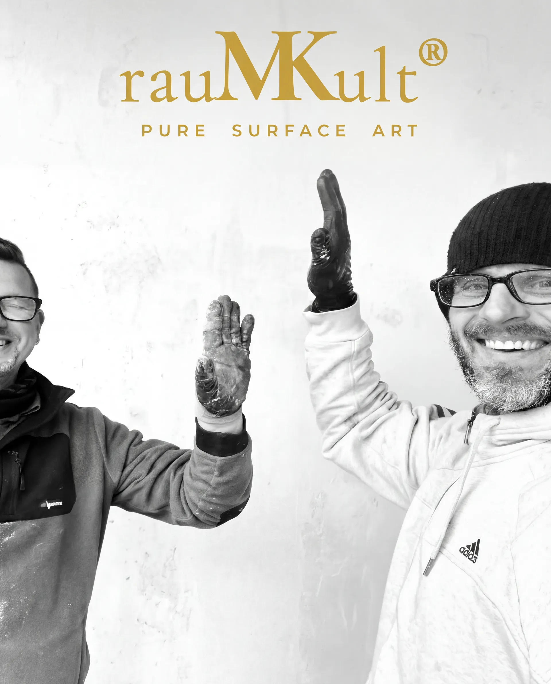 Das rauMKult-Team auf der Baustelle – lachend vor frisch bearbeiteter Betonwand mit rauMKult-Logo