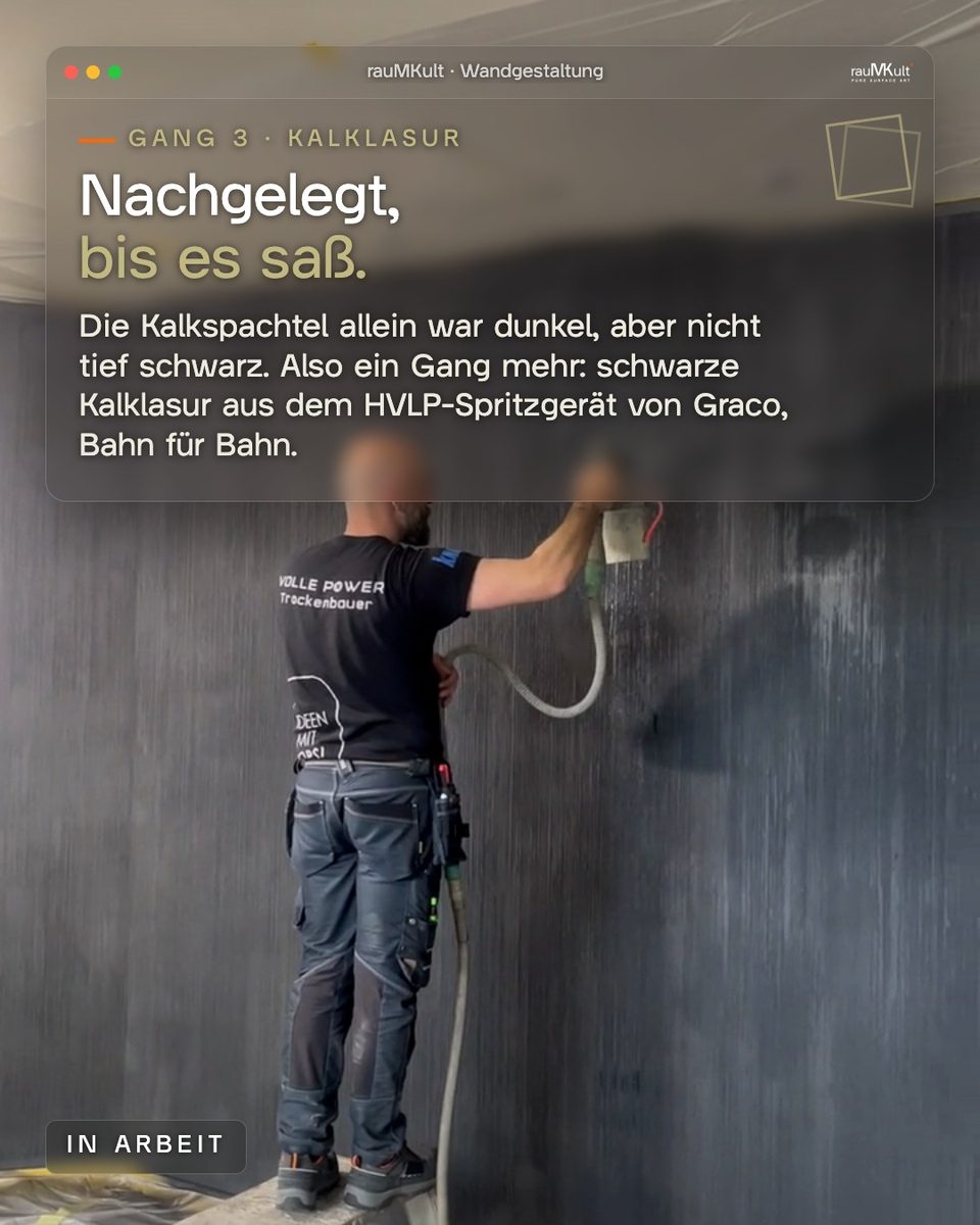 Gang 3: ein Handwerker von rauMKult spritzt schwarze Kalklasur mit dem HVLP-Spritzgerät auf die gerillte Wand