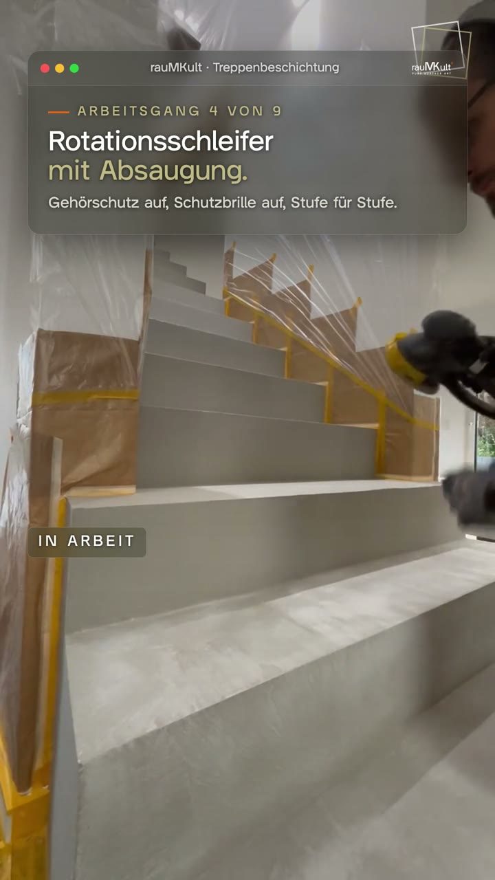 Hochkantvideo: die Stufen der Treppe aus Beton Ciré werden kniend mit dem Rotationsschleifer und Absaugung geschliffen, mit Gehörschutz und Schutzbrille