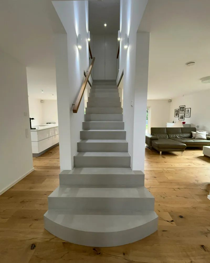 Reparierte Treppe aus Beton Ciré in Marl mit runder Antrittsstufe und Holzhandlauf, Blick vom Fuß der Treppe