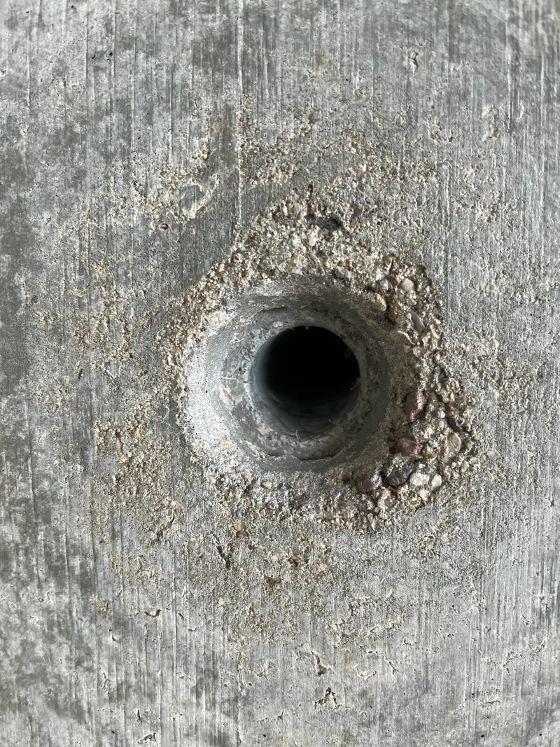 Ausgebrochener Ankerkonus in einer Sichtbetonwand, der Rand um das dunkle Loch ist rau und offen