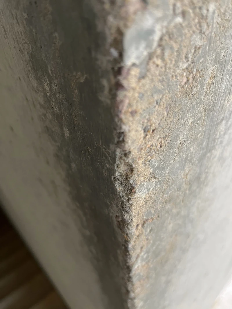 Abgeplatzte und ausgesandete Ecke an einem Vorsprung aus Sichtbeton, die Aussandung zieht vom Eck nach rechts in die Fläche