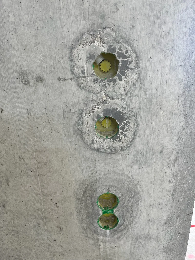 Drei Elektrodosen übereinander in der Sichtbetonwand, der Beton um die Aussparungen ist ausgeblutet und ausgewaschen