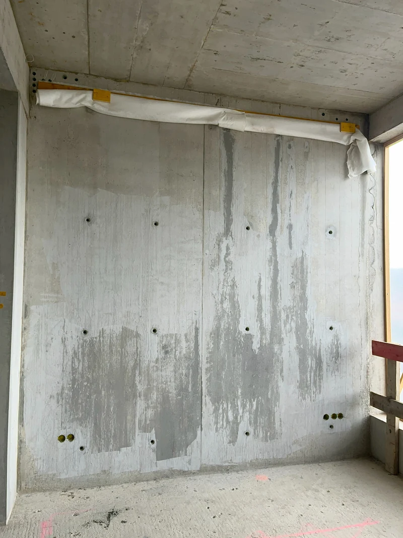 Große Sichtbetonwand nach der Grobkosmetik, die gefüllten Stellen zeichnen sich noch hell und dunkel ab