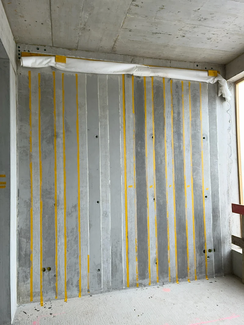 Erstes Rasterfeld der Wand im ersten Durchgang mit Feinspachtel, gelbe Bänder trennen die Bretter