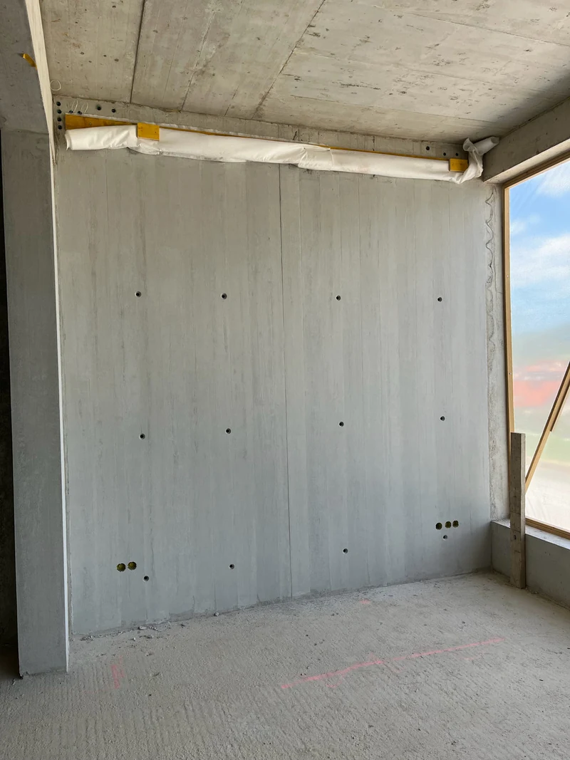 Die große Sichtbetonwand fertig, gleichmäßige Holzbrettstruktur mit Ankerkonen, Fenster rechts