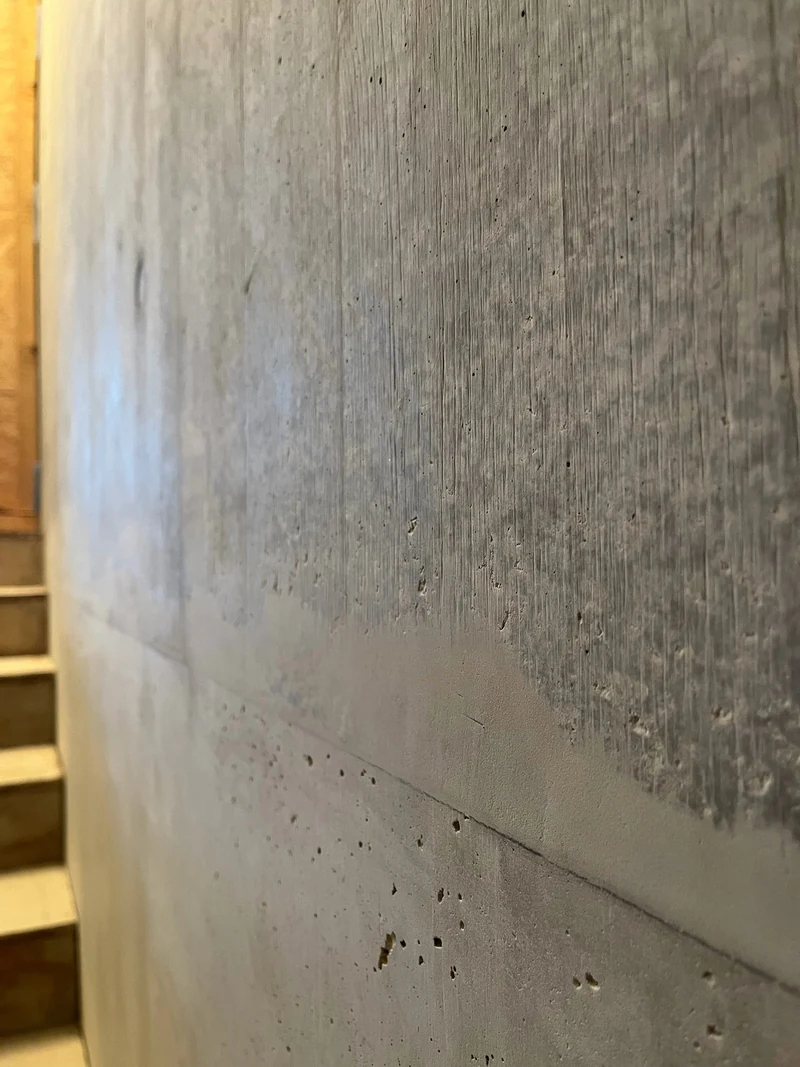 Treppenaufgang ins Untergeschoss mit Holzstufen, an der Fuge der Sichtbetonwand eine alte, helle Ausbesserung