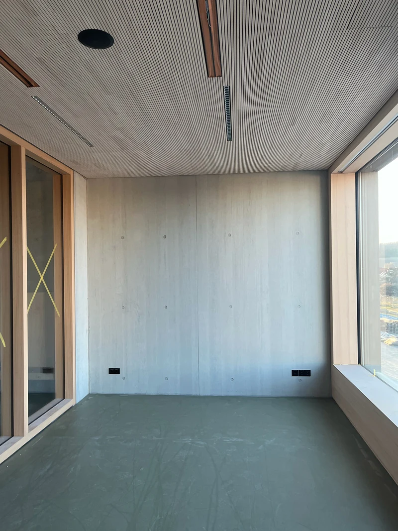 Fertiger Raum mit Holzlamellendecke und Holzfenstern, hinten die Sichtbetonwand mit durchlaufender Brettstruktur