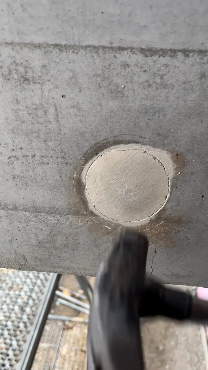 Ankerkonus mit hellem Pfropfen in einer dunkelgrauen Betonwand, darunter ein Gerüstbelag