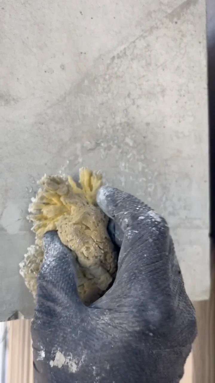 Retusche eines Ankerkonus mit einem Naturschwamm, Hand im Handschuh an der Betonwand