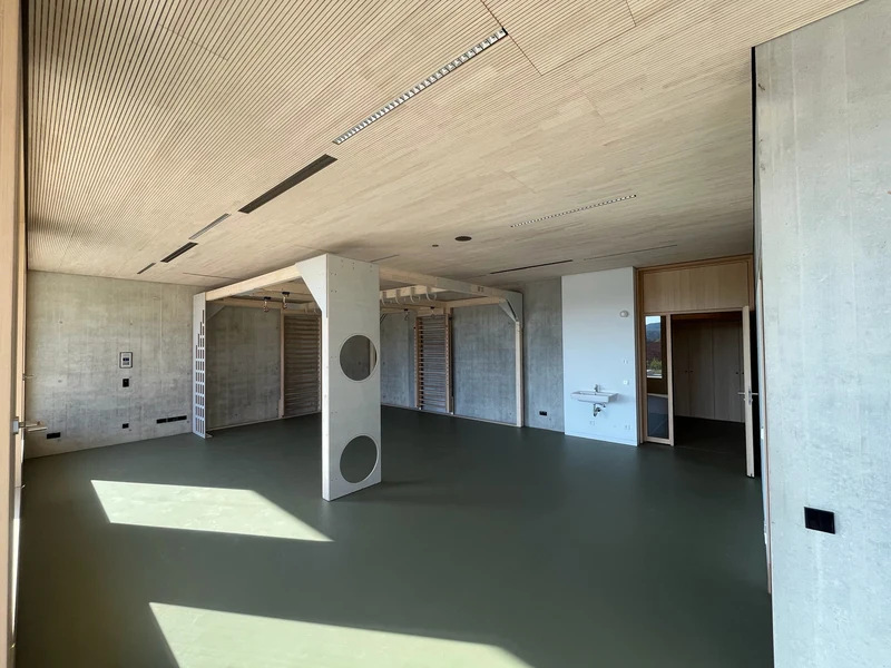 Sportraum im Weitwinkel, Wände mit viel Sichtbeton, durchgehende Holzdecke, in der Mitte der Holzeinbau der Kletterwand