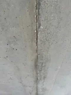 Senkrechte Schalungsfuge im grauen Sichtbeton mit feinen Lunkern und leichtem Grat entlang der Fuge