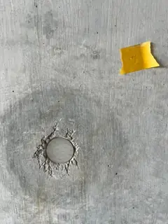 Ausgebrochener Rand um einen Ankerkonus im Sichtbeton, daneben gelbes Klebeband und ein dunkler Hof