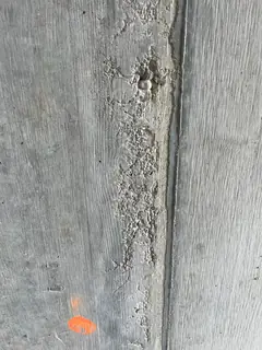 Kiesnest entlang einer Schalungsfuge mit freiliegenden Körnern, darunter eine orange Markierung