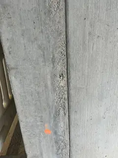 Raue, poröse Stelle entlang einer senkrechten Schalungsfuge an einer Kante, orange Markierung darunter