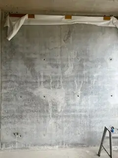Sichtbetonwand mit hellen Läufern und Ankerlöchern, oben weiße Abdeckung, rechts ein Gerüstteil