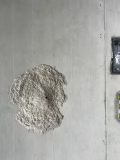Rundlicher Ausbruch mit rauer, heller Oberfläche und kleinem schwarzem Loch in der Mitte
