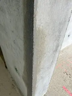 Betonkante mit dunklem senkrechtem Streifen entlang der Ecke, am Boden rosa Farbmarkierungen
