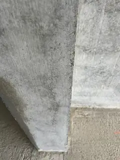 Unteres Ende einer Betonkante an einer Stütze, daneben glatte graue Wandfläche und Estrichboden