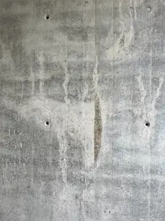 Linsenförmige, senkrechte Fehlstelle in einer Sichtbetonwand mit hellen Läufern und Ankerlöchern