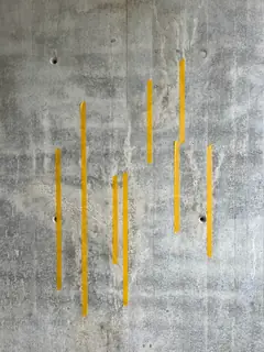 Sichtbetonwand mit mehreren senkrechten gelben Klebestreifen, die helle Läufer und Auswaschungen markieren