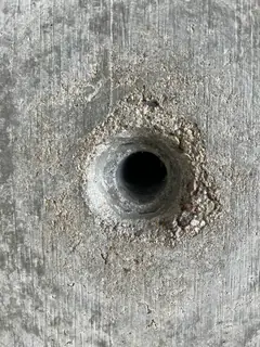 Tiefes dunkles Spindelloch, umgeben von einem Ring aus krümeligem, ausgebrochenem Beton
