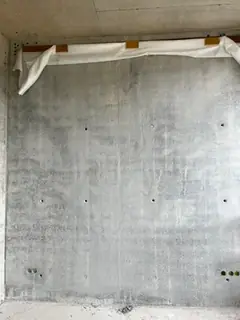 Glatte Sichtbetonwand mit kleinen Ankerlöchern, oben eine weiße Schutzabdeckung mit Klebeband