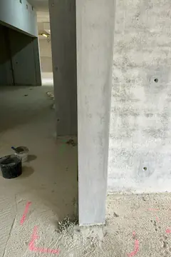 Betonstütze und Wand mit Ankerlöchern in einem Rohbauraum, am Boden rosa Markierungen und ein Eimer