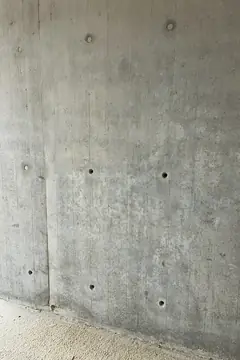 Sichtbetonwand mit senkrechter Plattenfuge und mehreren Ankerlöchern, unten ein Estrichboden