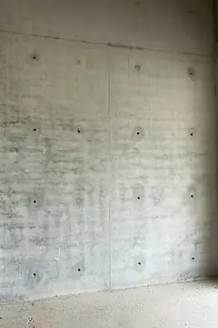 Sichtbetonwand mit gleichmäßig verteilten Ankerlöchern und zwei senkrechten Stößen, unten ein Boden