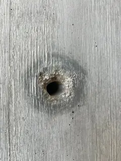 Spindelloch mit rostbraun verfärbtem, ausgebrochenem Rand in Sichtbeton mit deutlicher Brettmaserung