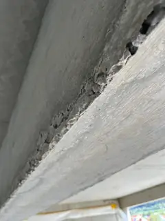 Betonkante von unten gesehen mit dunkler Hohlstelle und krümeligem, ausgebrochenem Material