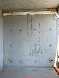 Sichtbetonraum mit zwei senkrechten Rissen, Ankerlöchern in der Wand und weißer Abdeckung unter der Decke
