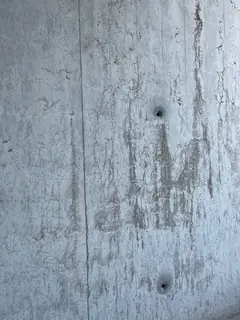 Sichtbetonwand mit senkrechten hellen Läufern und zwei kleinen Ankerlöchern, mittig eine feine Fuge