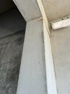 Betonstütze an einer Decke, daneben ein weißes Holzbrett und eine zusammengerollte weiße Schutzabdeckung