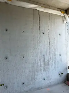Sichtbetonwand mit zwei senkrechten Rissen, mehreren Ankerlöchern und einer Abdeckung unter der Decke