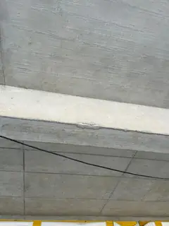 Blick auf einen Betonunterzug und eine Plattendecke mit Fugenraster, unten ein gelbes Gerüstteil