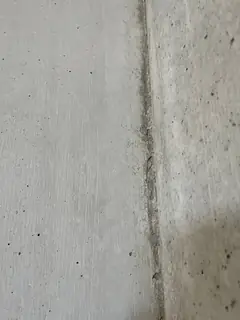 Senkrechte Schalungsfuge mit dunklem Streifen im Sichtbeton, daneben kleine Lunker