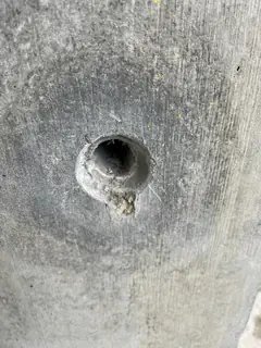 Dunkles Spindelloch mit kleinem Ausbruch am Rand, ringsum ein dunkler, runder Hof im Beton