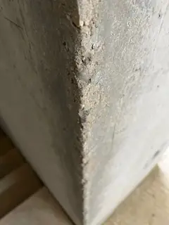 Betonkante mit körniger, abgesandeter Oberfläche über die ganze Höhe, unten eine Holzunterlage