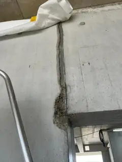 Dunkle senkrechte Fuge im Sichtbeton mit ausgebrochener, rauer Stelle am unteren Ende, links ein Handlauf